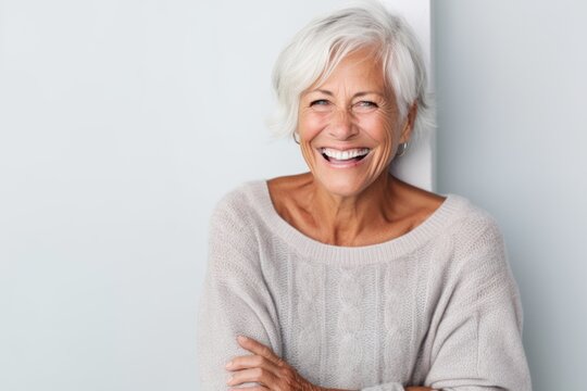 Portrait of smiling senior woman standing with arms crossed against white wall