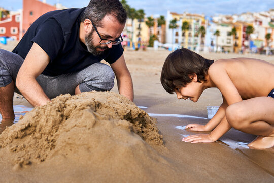 happy father and son playing with the sand on the beach in summer