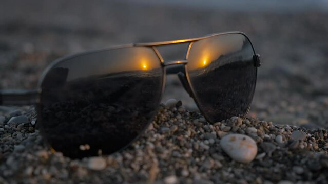 Black sunglasses on pebbles shore. A view of sunny beach with left sunglasses on the pebbles bay in sun rays in the evening.