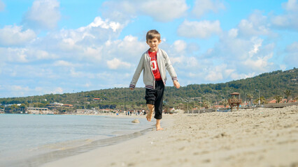 Happy laughing boy running on the sandy sea beach. Concept of tourism, travel, summer vacation