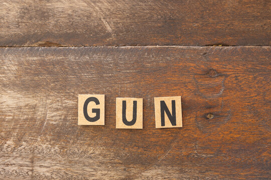 The word gun formed with wooden blocks on a rustic background.
