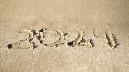 Calm sea waves washing off 2024 new year written on wet sand