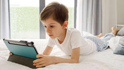 Young boy enjoys screen time in his bed, using a tablet computer to explore the digital world. Child using gadget, education and development.