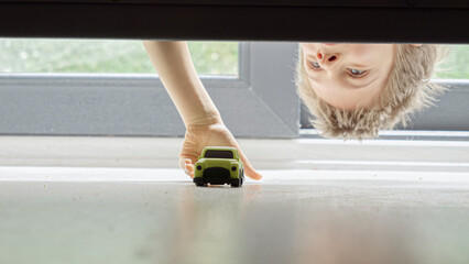 Little boy searching and taking his toy car lost under the bed