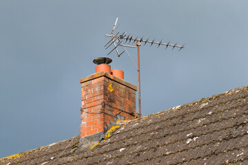 Television antenna on brick chimney above tiled roof to receive TV signals over the air