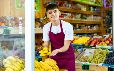 Obraz premium Young man employees in uniform lay out and selling organic banana in grocery shop
