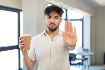 young handsome man looking serious showing open palm making stop gesture. take away coffee concept