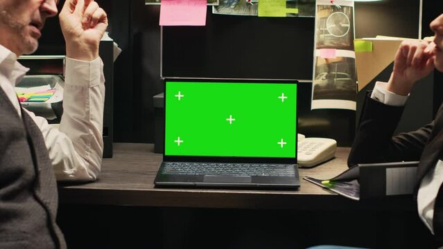 Inspectors review greenscreen on laptop, working together in incident room. Police officers looking at chromakey display with isolated template, evaluating forensic evidence and proof.