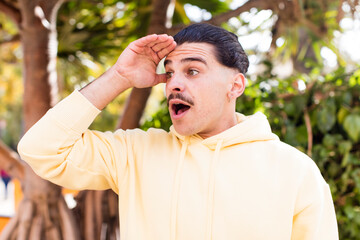 young cool man looking bewildered and astonished, with hand over forehead looking far away, watching or searching