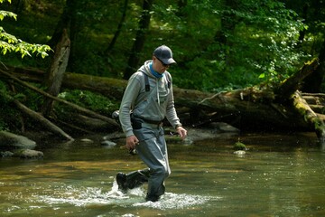 Fisherman crossing river with spinning rod in his hands. Trout fishing.