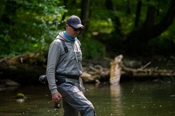 Fisherman crossing river with spinning rod in his hands. Trout fishing.