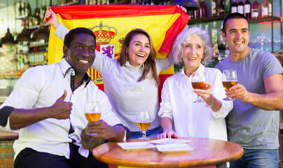 Obraz na płótnie Canvas Diverse group celebrating with Spanish flag at a pub with beer..