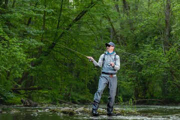 Fisherman catching brown trout on the fly standing in river.