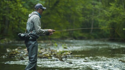 Fisherman catching brown trout on the fly standing in river.