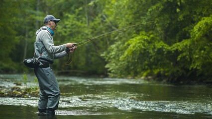 Fisherman catching brown trout on the fly standing in river.