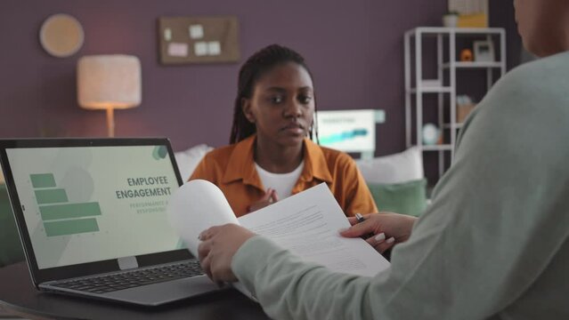 Female hr manager reading employee contract to young Black woman during job interview in modern marketing office