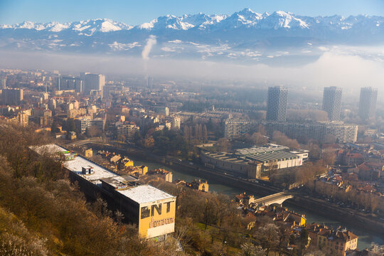 Picturesque mountains landscape of snowy Alps and center of Grenoble under clouds in sunny winter day