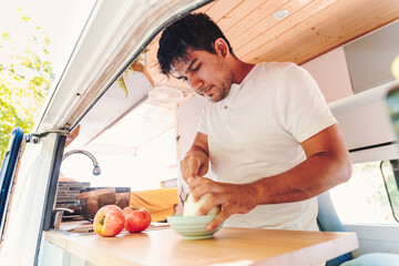 Man cutting vegetables for meal in the kitchen of his camper van. Van road trip holiday and outdoor summer adventure. Nomad lifestyle concept