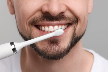 Naklejka premium Man brushing his teeth with electric toothbrush on light grey background, closeup