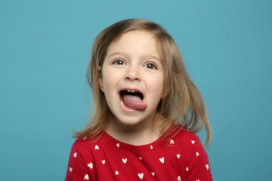 Funny little girl showing her tongue on light blue background