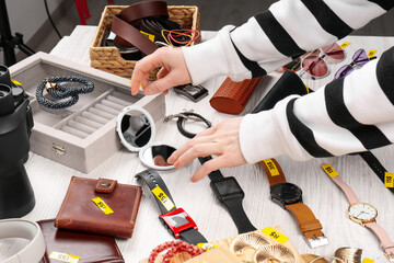 Woman choosing something at white wooden table with different stuff indoors, closeup. Garage sale