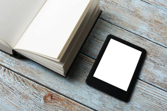 Portable e-book reader and hardcover book on wooden rustic table