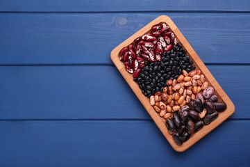 Plate with different kinds of dry kidney beans on blue wooden table, top view. Space for text