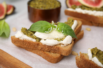 Tasty bruschetta with cream cheese, pesto sauce and fresh basil on parchment paper, closeup