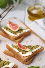 Tasty bruschetta with cream cheese, pesto sauce and fig on parchment paper