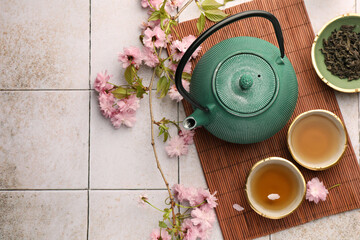 Traditional ceremony. Cup of brewed tea, teapot, dried leaves and sakura flowers on tiled table,...