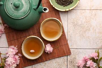 Traditional ceremony. Cup of brewed tea, teapot, dried leaves and sakura flowers on tiled table, flat lay with space for text