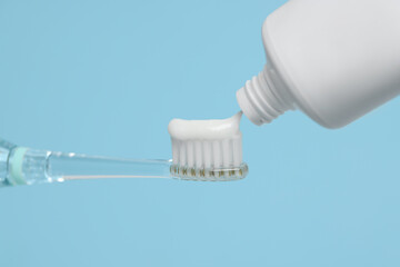 Fototapeta na wymiar Squeezing toothpaste onto electric toothbrush on light blue background, closeup