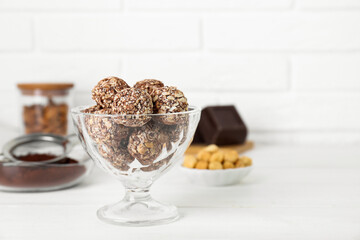 Glass dessert bowl of tasty chocolate balls on white wooden table, closeup. Space for text