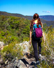 A beautiful girl celebrates a successful climb of the Pages Pinnacle and enjoys the view while standing on the narrow Razorback ridge. Hidden gems in Springbrook National Park, Gold Coast, Queensland 