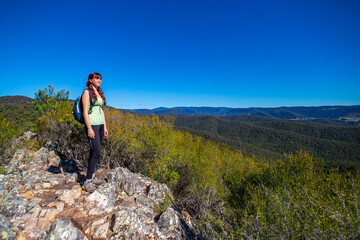 Obraz premium A beautiful girl celebrates a successful climb of the Pages Pinnacle and enjoys the view while standing on the narrow Razorback ridge. Hidden gems in Springbrook National Park, Gold Coast, Queensland 