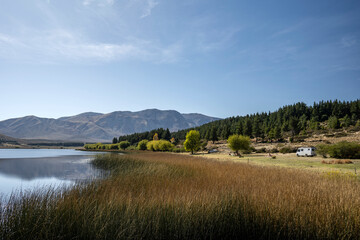 View of Laguna Zeta, with. reeds in the foreground and mountains behind and a motorhome on the side, in Esquel, Chubut, Argentine Patagonia.
