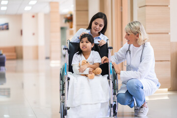 Obraz premium Female pediatrician doctor and child patient on wheelchair with her mother in the health medical center