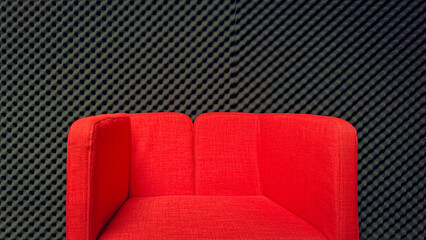A red sofa is placed in a studio room with a background of egg crate foam