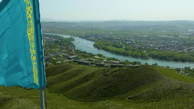 flying past flag of Republic of Kazakhstan with view on city of East Kazakhstan River, Ust Kamenogorsk. Observation deck on mountain Kazakhstan Summer sunny day.
