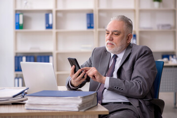 Fototapeta na wymiar Old male employee speaking by phone at workplace