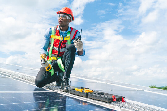 African American engineer maintaining solar cell panels on factory building rooftop. Technician working outdoor on ecological solar farm construction. Renewable clean energy technology concept