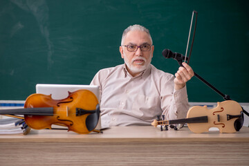 Old male teacher playing violin in the classroom