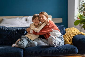 Little kid boy cuddling older sister at home. Happy American siblings hugging embracing feeling love, care, connection. European family showing love. Small brother with teen girl in closes relations. 
