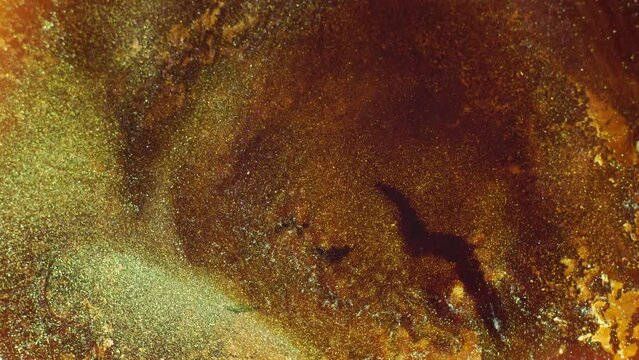 Ochre yellow shiny gold liquid glitter makeup texture. Brilliant abstract background macro. Motion mixed glistening colorful ink