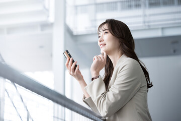 Fototapeta premium オフィスでスーツ姿でスマホ持つ転職などを迷ったり考える美人な女性 コピースペース