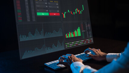 Caucasian man sits in the dark in front of a virtual screen. Stock exchange charts. Close-up of male hands on the keyboard.