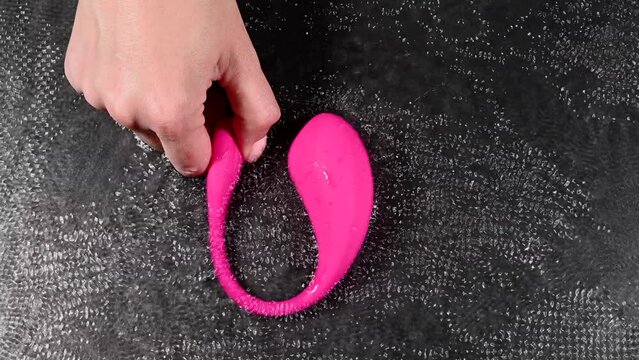 A woman is holding a pink vibrator in water. Sex toy on a black background. Different modes and speeds of vibration.