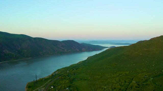 aerial footage of rippling waters of Bukhtarma Reservoir with stunning orange sunset with lush green trees and majestic mountain ranges near ust Kamenogorsk
