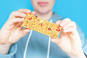 Young woman holding protein bar on blue background, selective focus.