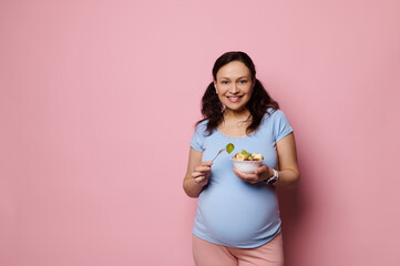 Isolated studio portrait on pink background of a multi ethnic dark-haired beautiful pregnant woman,...